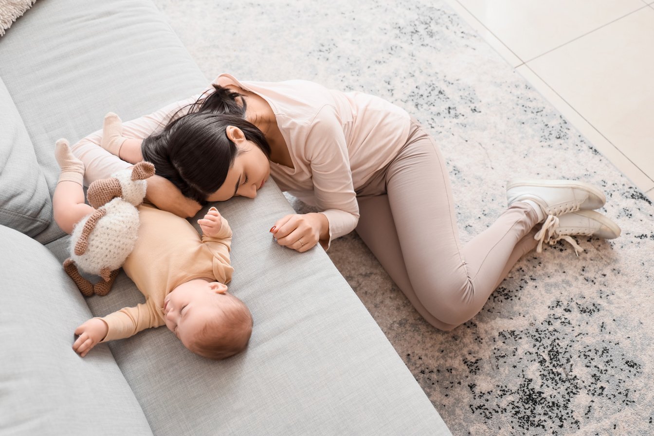 Sleeping Young Woman with Her Baby on Sofa Suffering from Postnatal Depression at Home